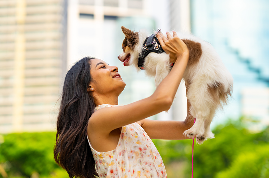 Young Filipino woman lovingly holding up her small pet dog outdoors, representing the growing pet parenting trend in the Philippines.