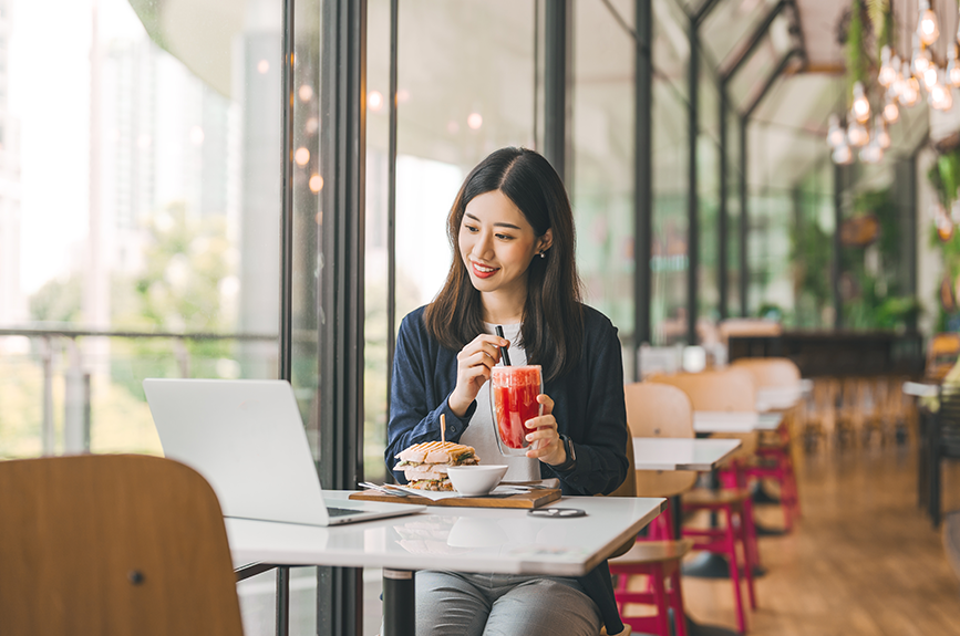 A young Filipino woman sitting alone at a modern café, enjoying her meal while watching something on a laptop. It represents how younger generations are starting to enjoy doing things alone, including living solo.
